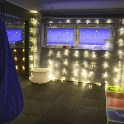 Pokój wyciszenia: przygaszone światła, zawieszony kokon, świetlne girlandy i kolorowe płytki podłogowe.